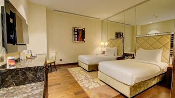 A hotel room with a marble reception desk, two beds with headboards, a large mirror, and a wooden floor.