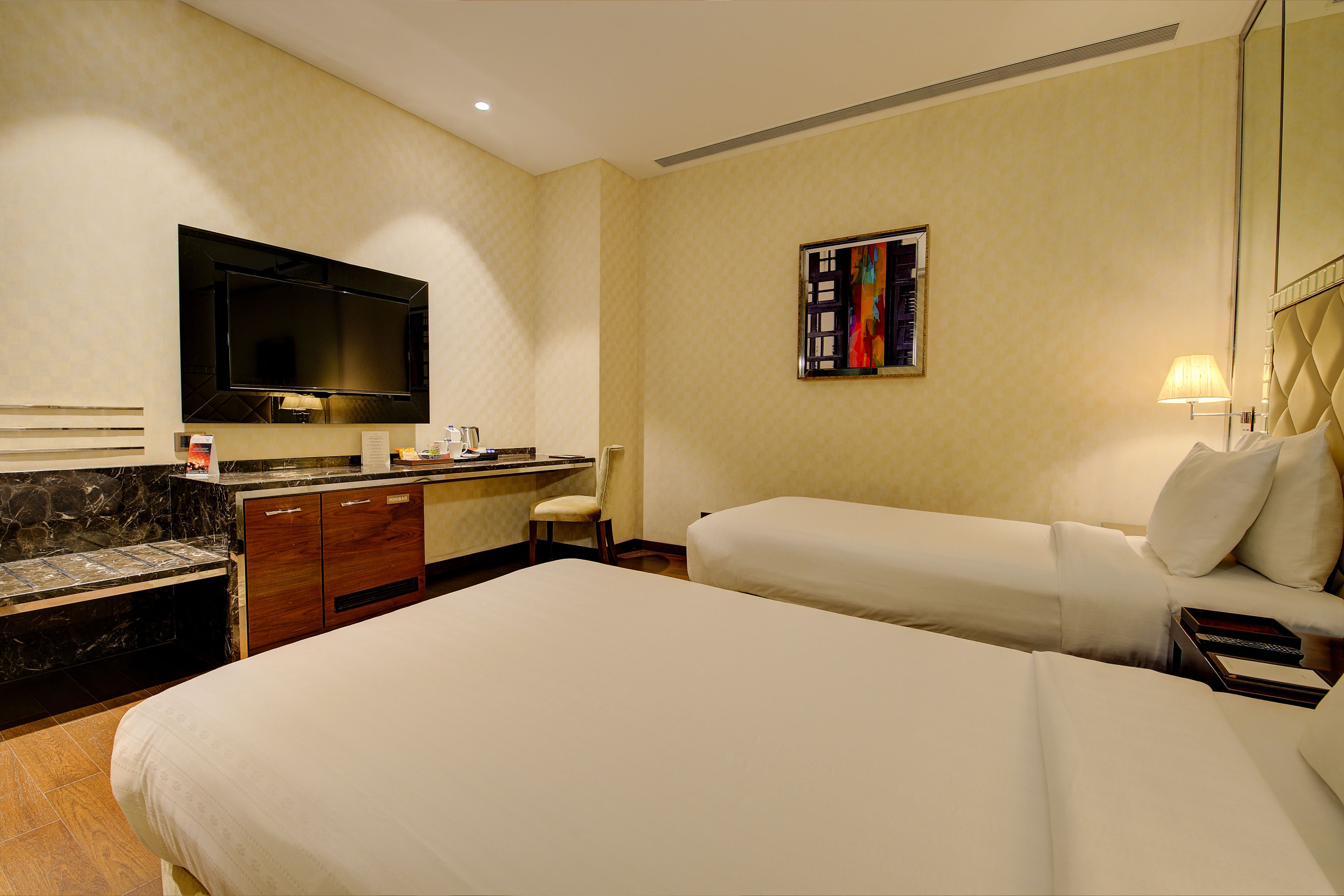 Una habitación de hotel con dos camas, un escritorio, un televisor y un cuadro en la pared.