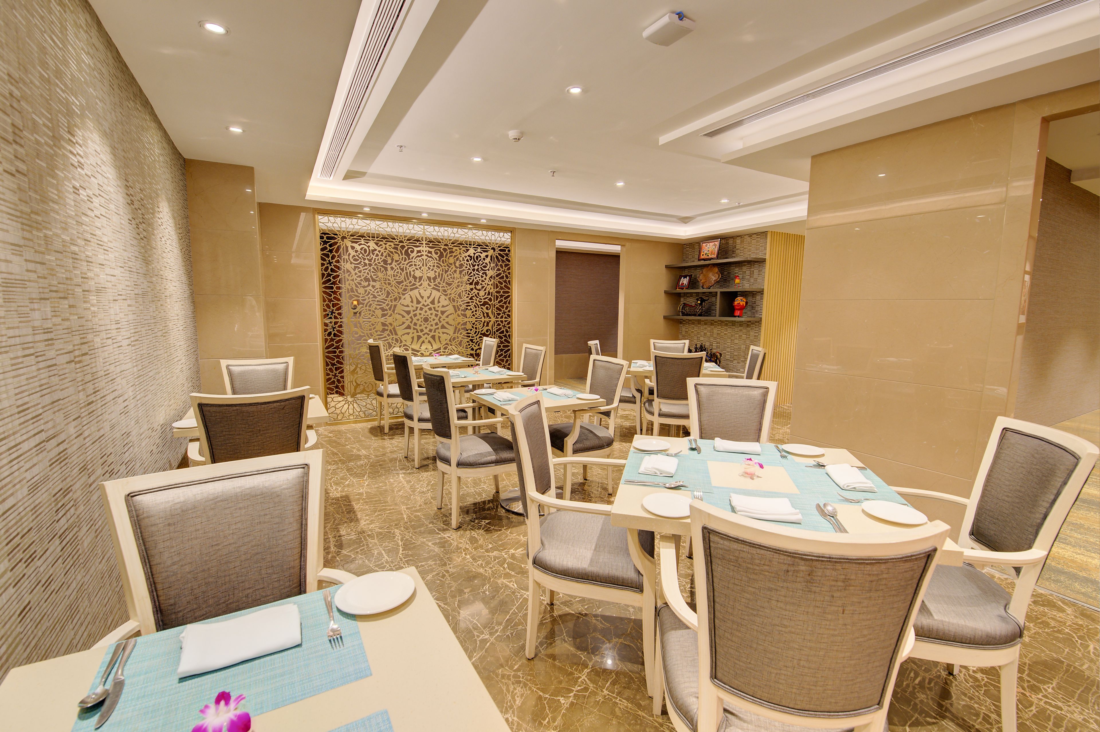 A hotel dining area with multiple tables and chairs, a patterned wall, and a decorative screen.