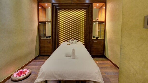 A hotel room with a long bed, wooden paneling, and a decorative wall with a geometric pattern.