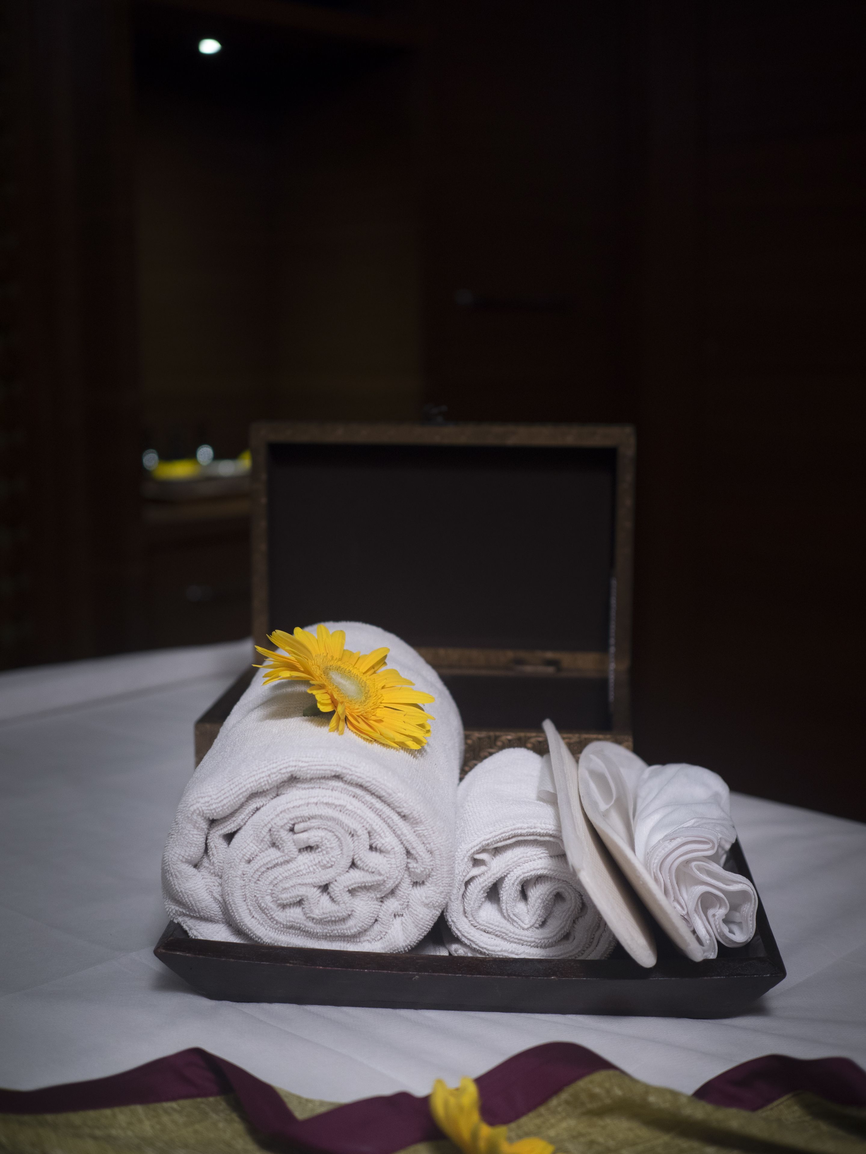A neatly arranged set of towels and a flower on a tray in a dimly lit room.