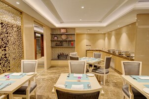 A hotel dining area with tables set for four, a buffet line, and decorative wall art.