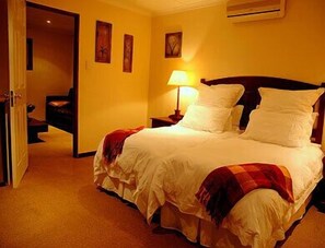 A hotel room with a bed, a nightstand, a lamp, and a door leading to another room.