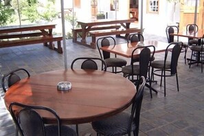 An outdoor dining area with round tables and chairs, benches, and a tiled floor.
