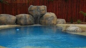Una piscina con una cascada y una valla de bambú al fondo.