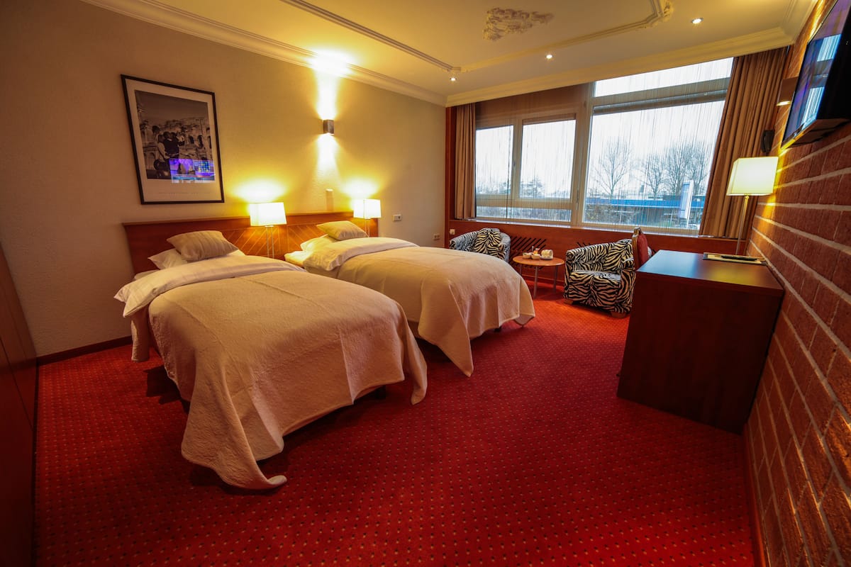 A hotel room with two beds, a desk, a chair, and a large window.