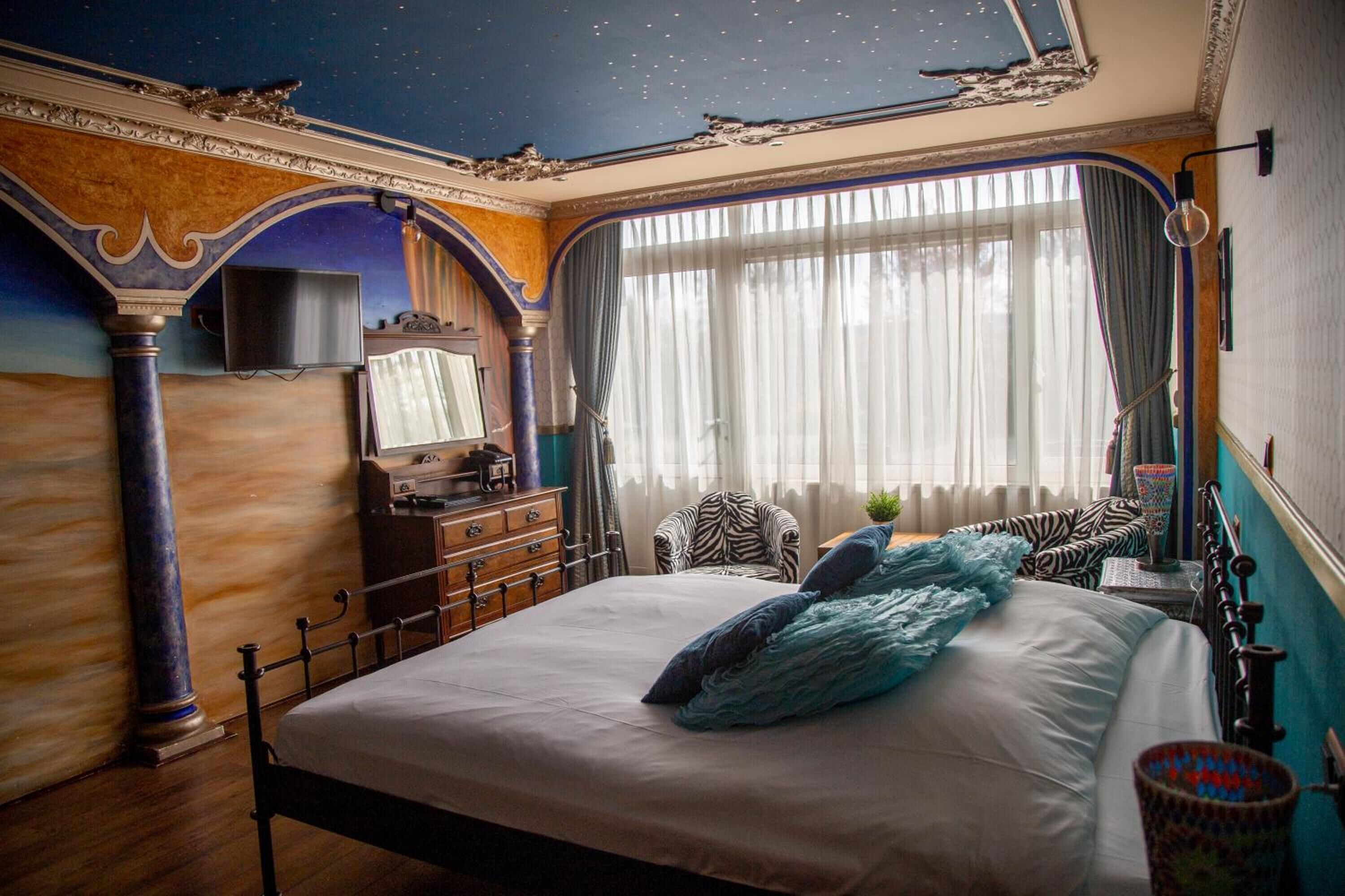 A bedroom with a bed, a desk, a chair, a television, and a window with curtains.