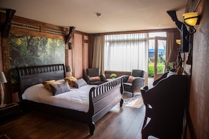 Un dormitorio con una cama grande, dos sillones, una mesita y vistas al exterior.