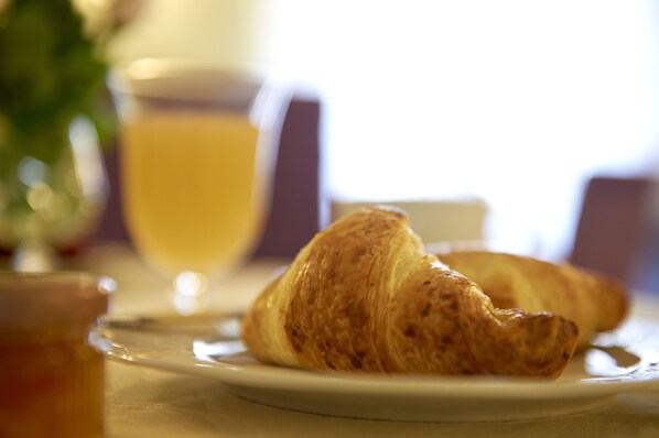 Um croissant num prato, com um copo de sumo de laranja ao fundo.