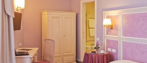 A hotel room with a bed, a desk with a laptop, a chair, a wardrobe, and a bathroom visible through an open door.