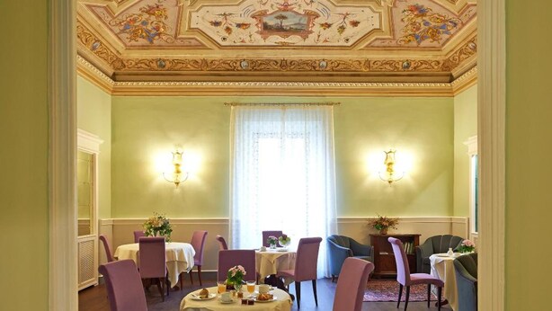 Comedor con techo alto que presenta frescos ornamentales, un candelabro y un amplio ventanal con cortinas.