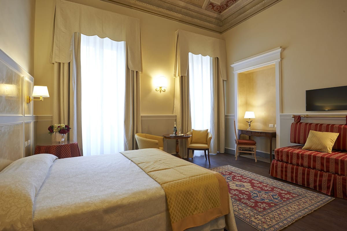 A hotel room with a large bed, a desk, a chair, and a sofa.