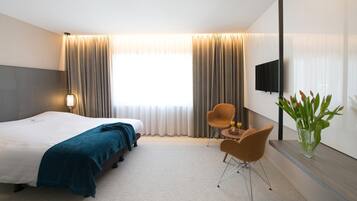 Een hotelkamer met een bed, twee stoelen, een televisie en een vaas met bloemen.