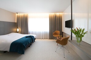 A hotel room with a bed, two chairs, a TV, and a vase with flowers. - Hotel Princess (Ostend)