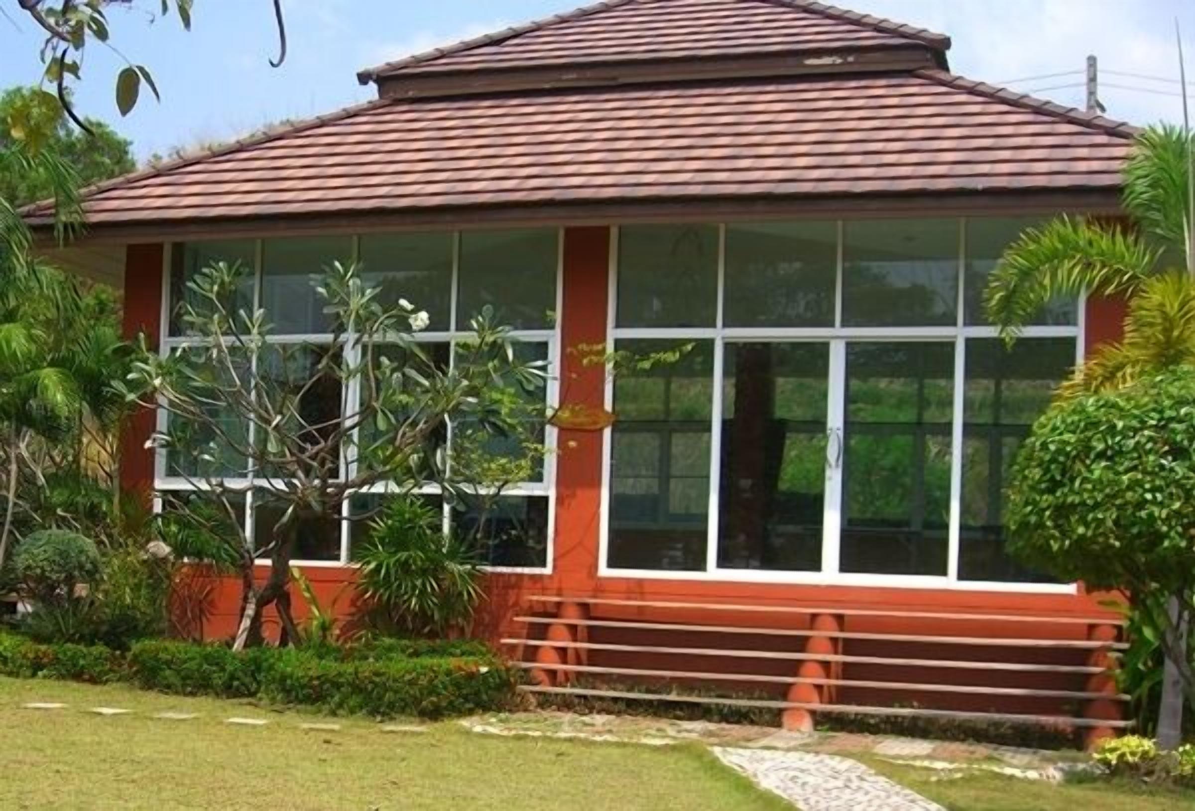 A building with a red roof and large windows, surrounded by greenery.