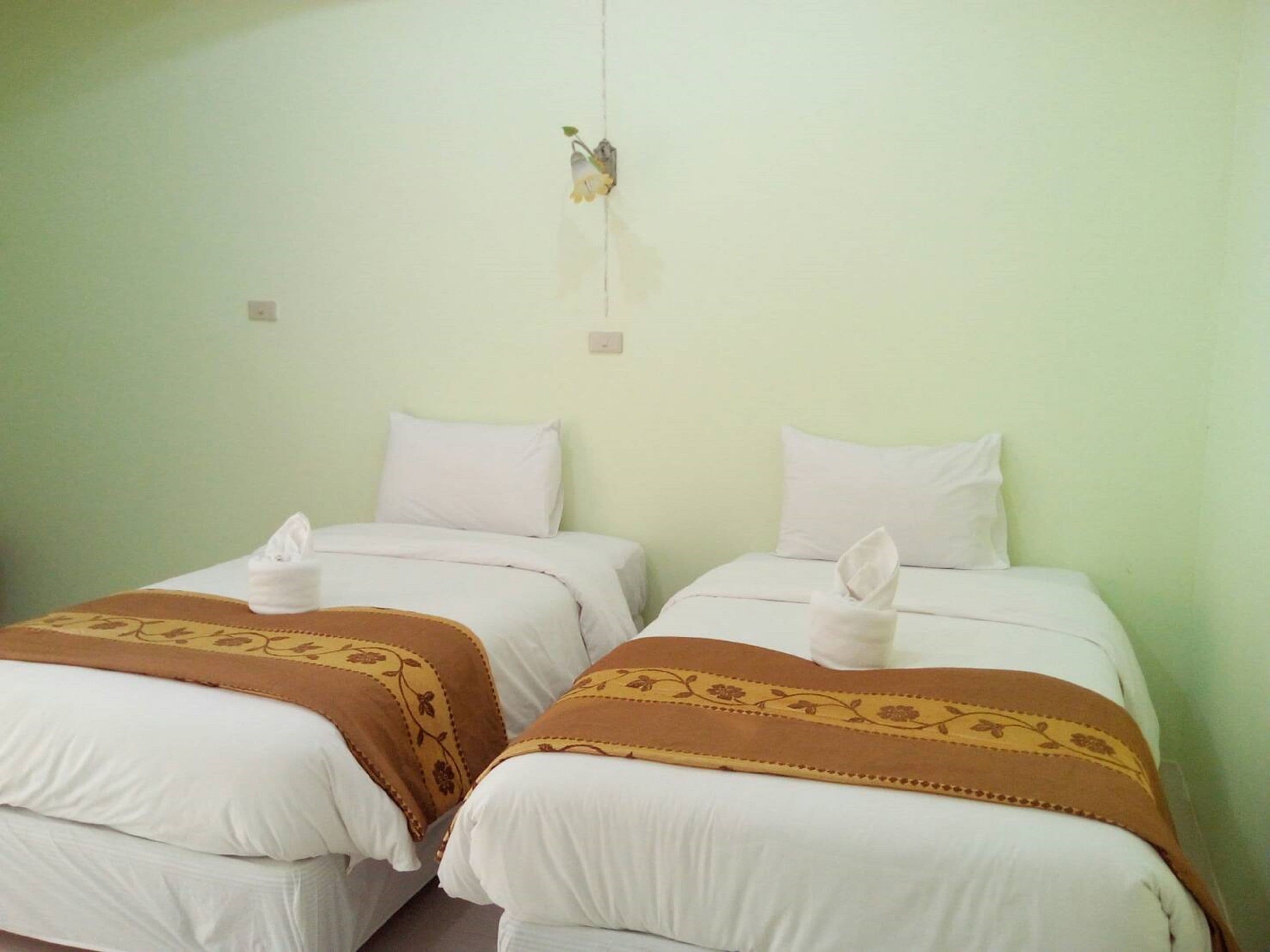 Two single beds with white linens and brown decorative borders, a light green wall, and a small wall-mounted light fixture.