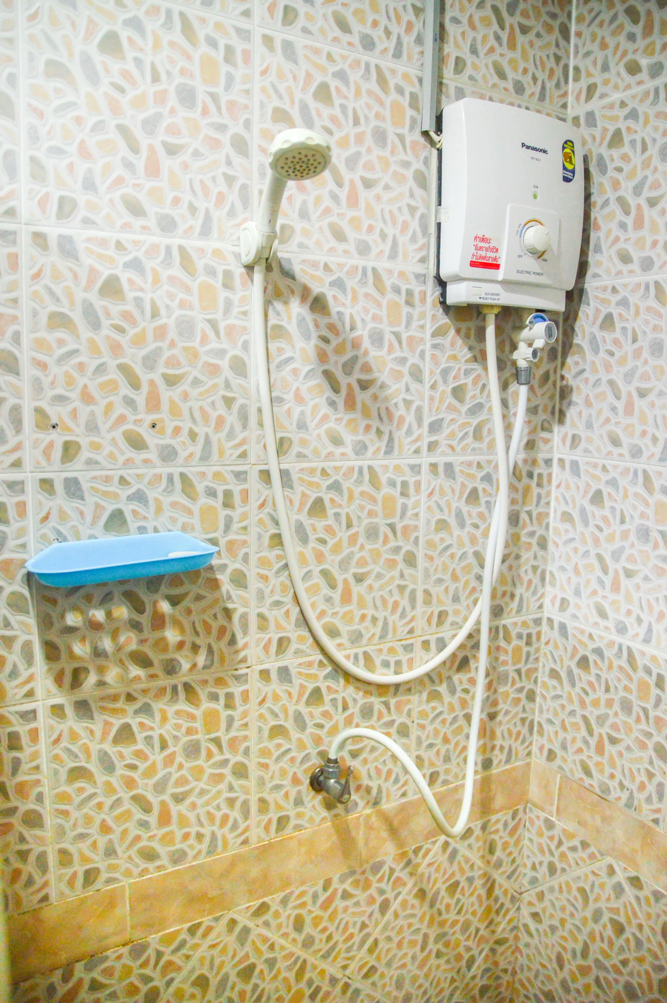 A bathroom with mosaic tile walls, a handheld showerhead, and a wall-mounted electric heater.