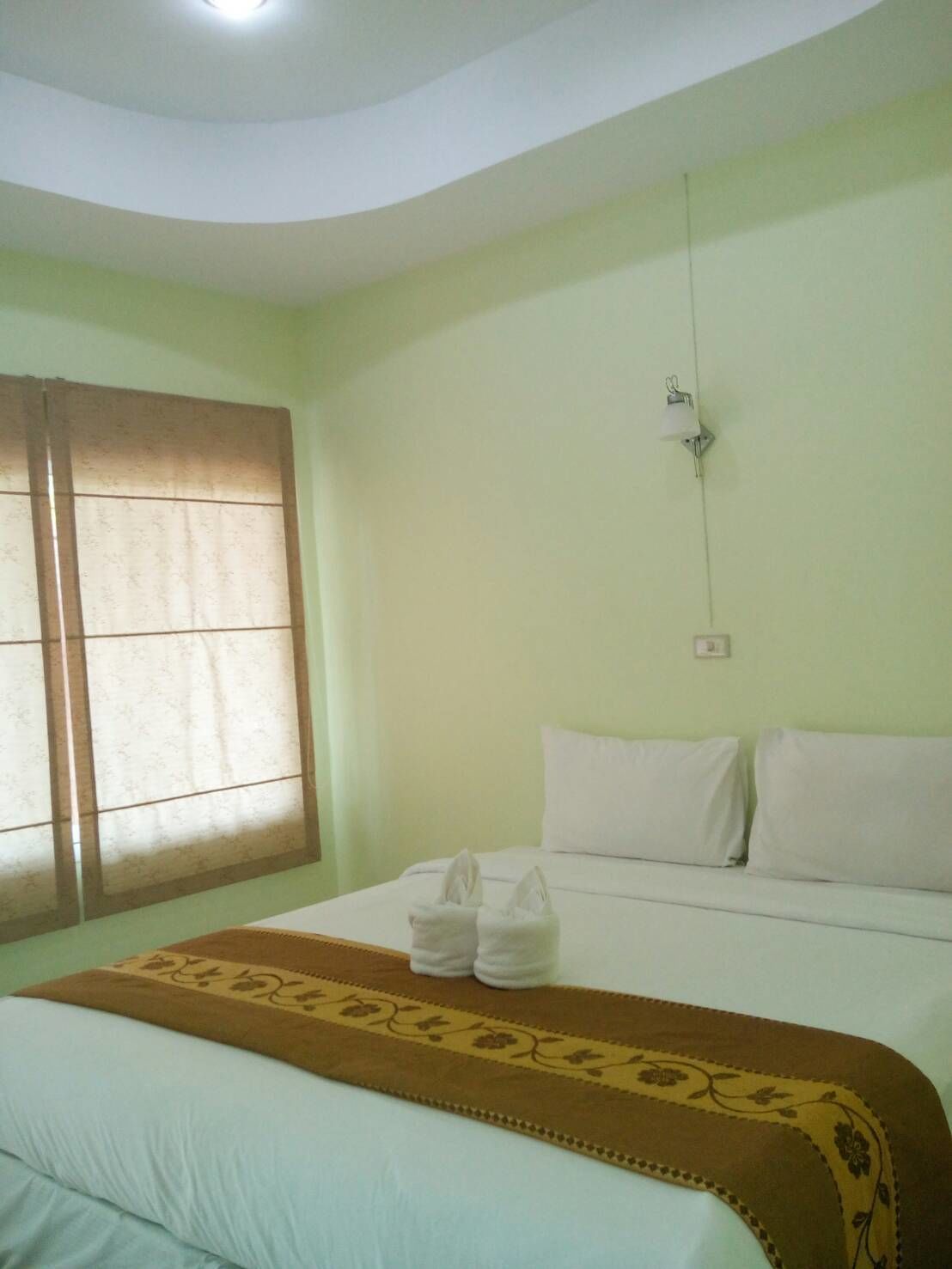 A hotel room with a bed, a window with curtains, a wall clock, and a bedside table with towels.
