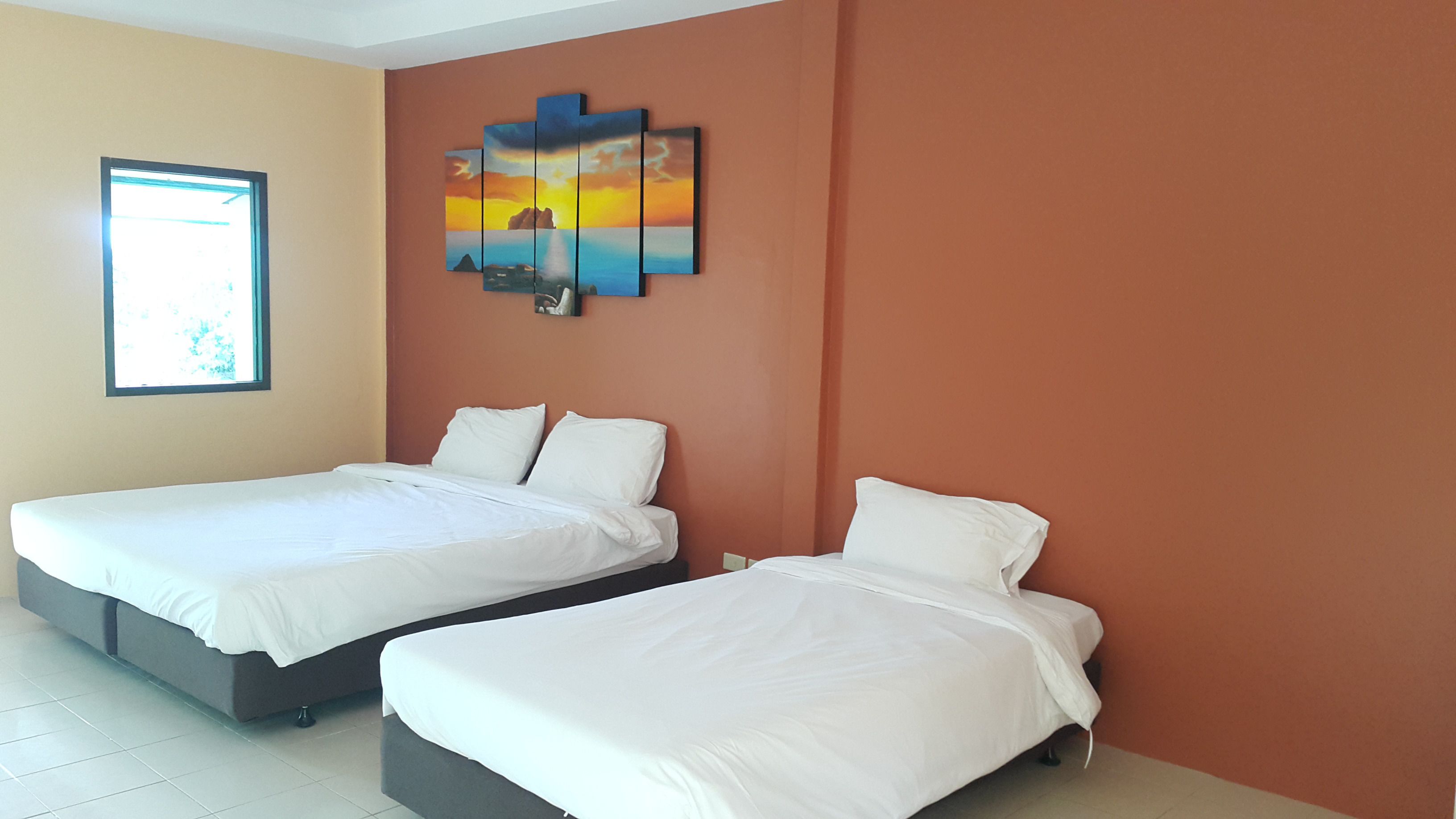 Une chambre d’hôtel avec deux lits simples, une grande fenêtre et un tableau représentant un coucher de soleil au mur.