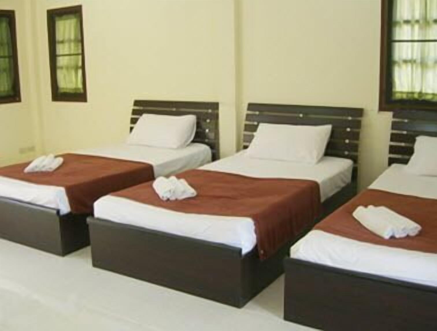 A hotel room with three single beds, each with a brown headboard and white bedding.