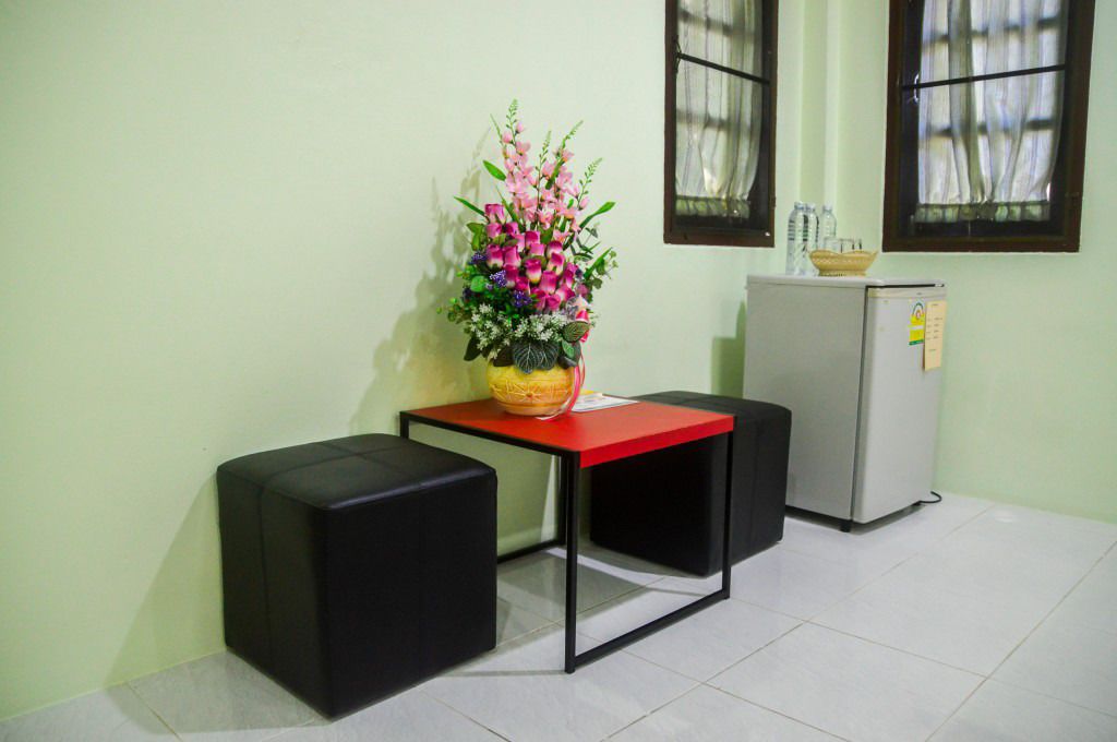 A small room with a red table, two black chairs, a white refrigerator, and a flower arrangement on the table.