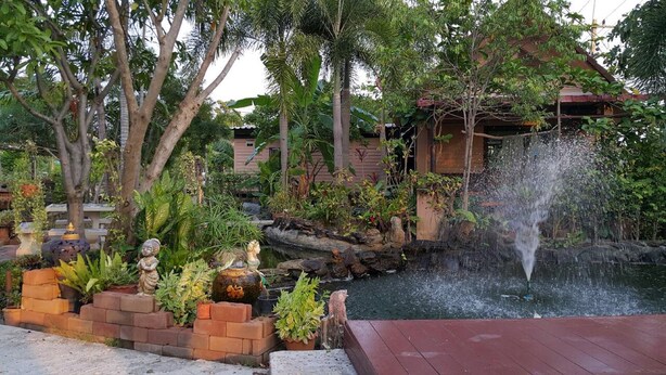 Un jardín con fuente de agua, estatuas de piedra y una terraza de madera.