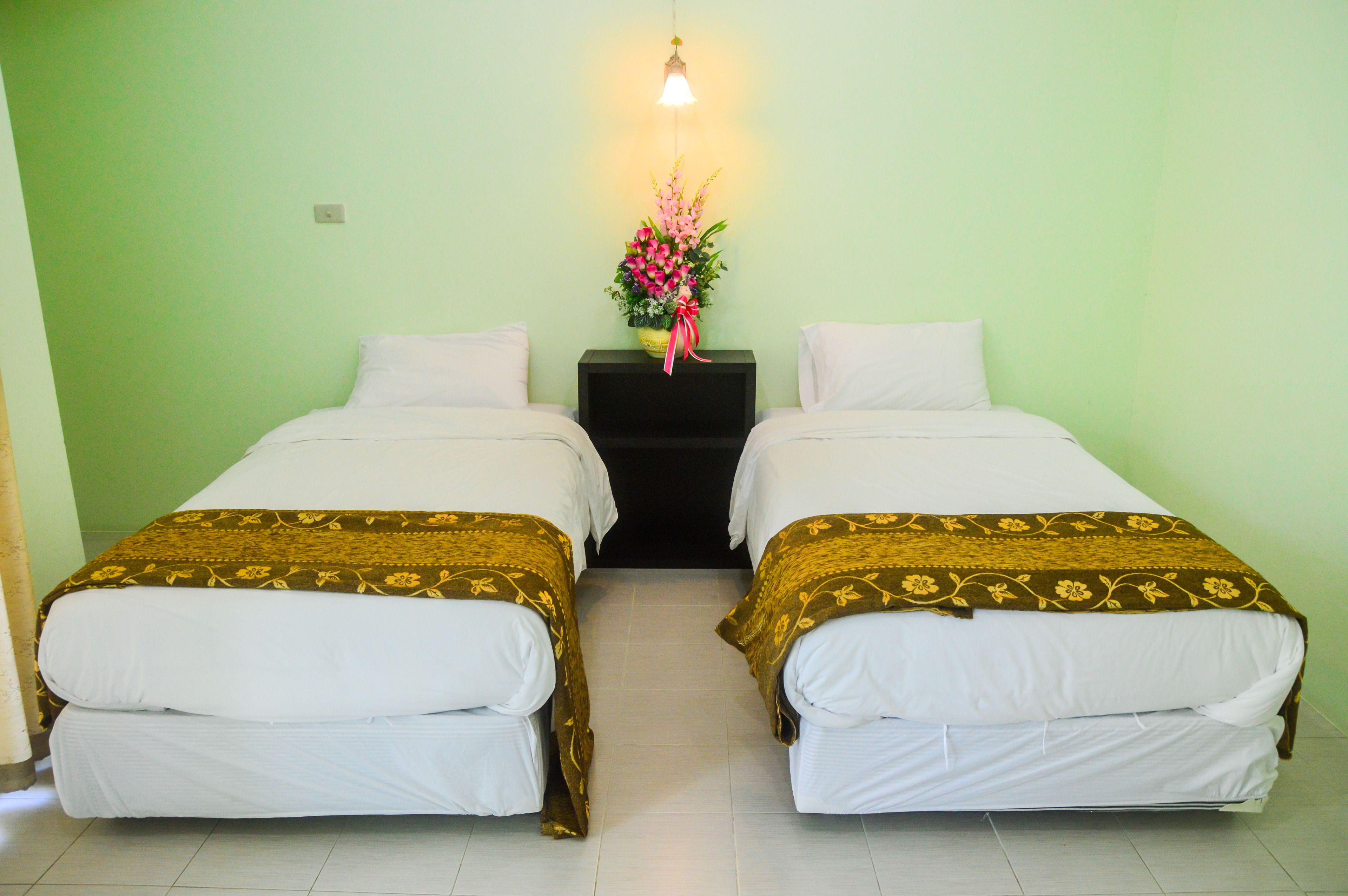 A room with two beds, each with a patterned bedspread and white linens. There is a nightstand with a vase of flowers between the beds.
