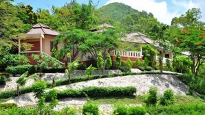 Un resort tropical con varias edificaciones tipo bungalow rodeado de exuberante vegetación y montañas al fondo.