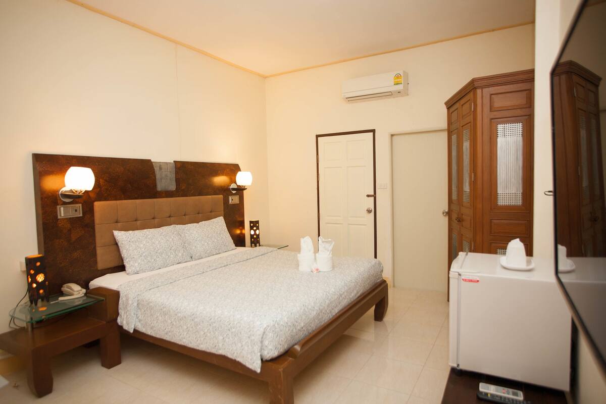 Ein Hotelzimmer mit Bett, Nachttischlampen, einem Nachttisch, einem Kühlschrank und einem Kleiderschrank.