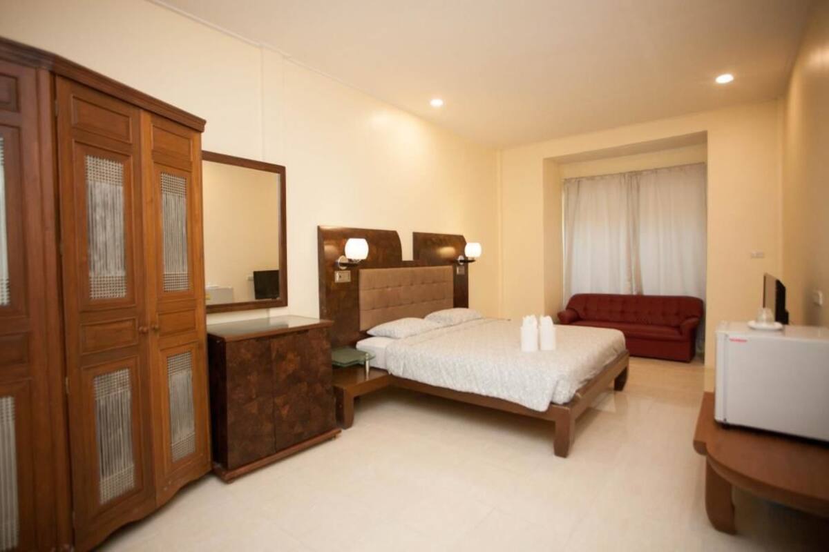 Ein Hotelzimmer mit einem Bett, einem Holzschrank, einem Schreibtisch, einem roten Sofa und einem Fenster mit Vorhängen.