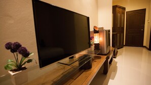Un televisor de pantalla plana sobre un estante de vidrio, una pequeña planta en maceta y un mueble de madera en una habitación bien iluminada.