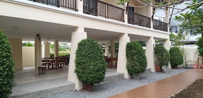 A covered outdoor area with a seating arrangement, potted plants, and a balcony. - Lotusland Resort (Pattaya)