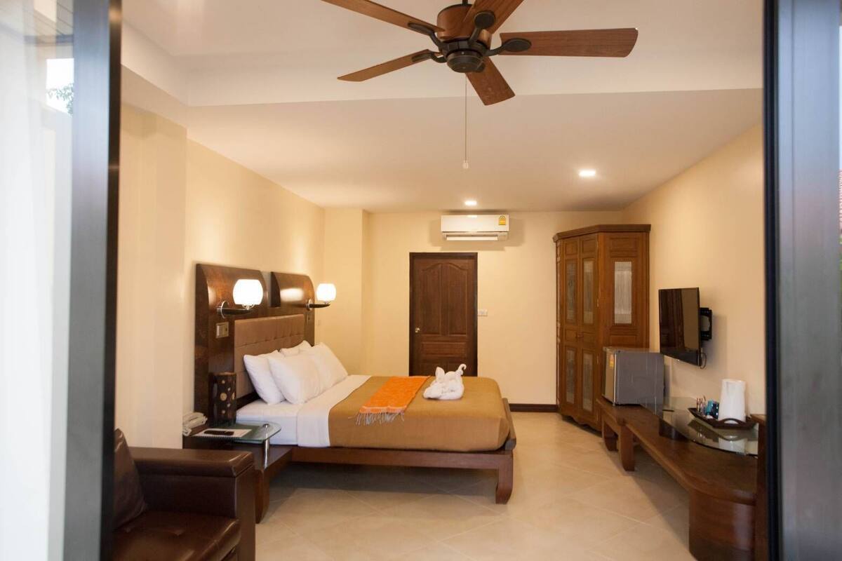 Ein Hotelzimmer mit Bett, Schreibtisch, Kleiderschrank, Deckenventilator und Klimaanlage.