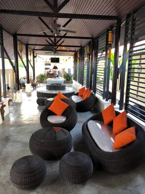 A covered outdoor seating area with round, cushioned seating and orange pillows, a ceiling fan, and a television screen. - Lotusland Resort (Pattaya)
