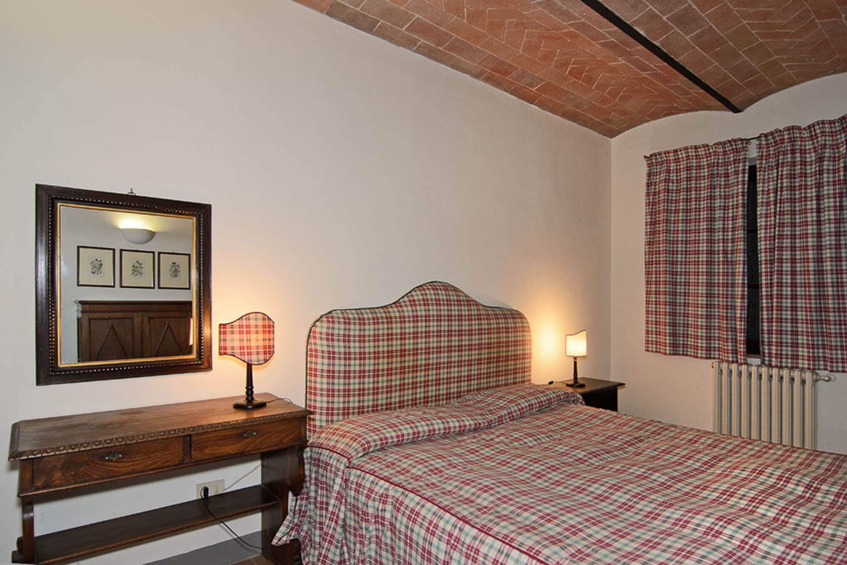 A bedroom with a checkered bedspread, a wooden dresser, a mirror, and a radiator.