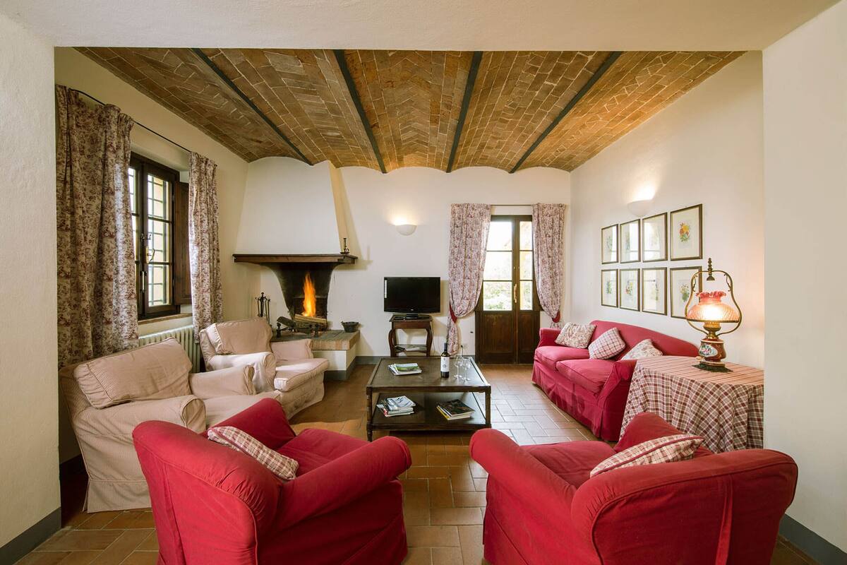 Ein Wohnzimmer mit roten Sofas, einem Kamin, einem Fernseher und einem Tisch mit Büchern.