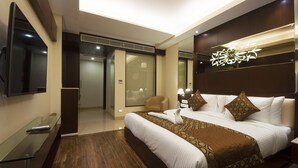 A modern hotel room with a large bed, a flat-screen TV, a glass desk, and a sliding door leading to a bathroom. - Hotel Golden Grand (New Delhi)