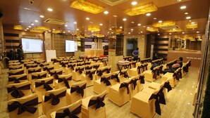 A conference room with rows of chairs, a podium, and a presentation screen. - Hotel Golden Grand (New Delhi)