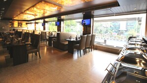 A restaurant with a modern interior, featuring a long counter with multiple seating options, including booths and individual tables. - Hotel Golden Grand (New Delhi)