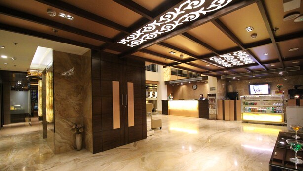 A hotel lobby with a marble floor, a reception desk, and a bar area. - Hotel Golden Grand (New Delhi)