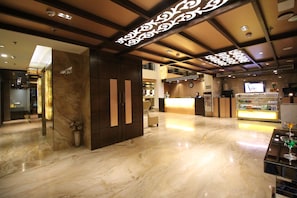 A hotel lobby with a marble floor, a reception desk, and a bar area.