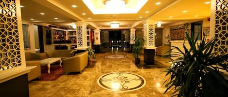 A hotel lobby with a marble floor, sofas, a coffee table, and decorative plants.