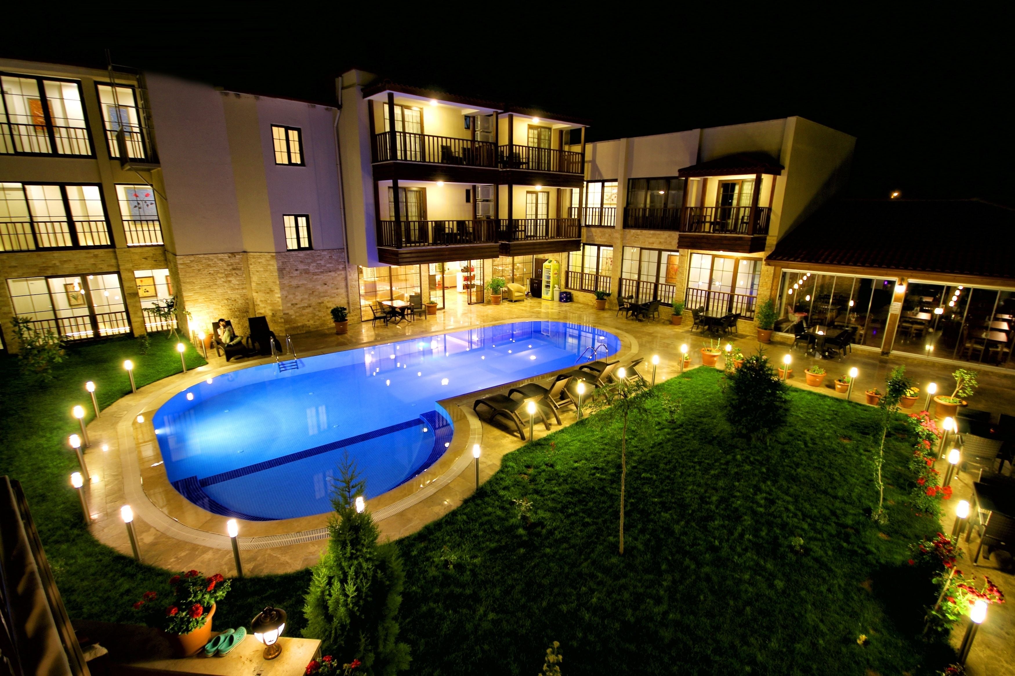 A hotel with a swimming pool, outdoor seating, and a well-lit garden area.