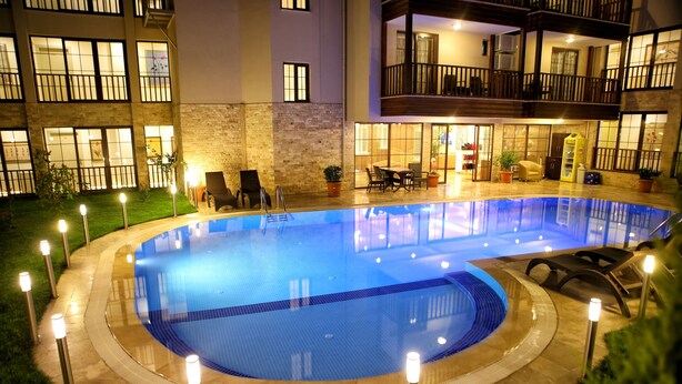 A swimming pool with a circular design, surrounded by a stone deck and illuminated by ground lights. - Venus Suite Hotel (Denizli)