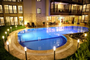Una piscina de diseño circular, rodeada por una terraza de piedra e iluminada por luces empotradas.