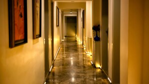 A long, well-lit hallway with framed artwork on the walls, leading to a door with a vase of flowers. - Venus Suite Hotel (Denizli)