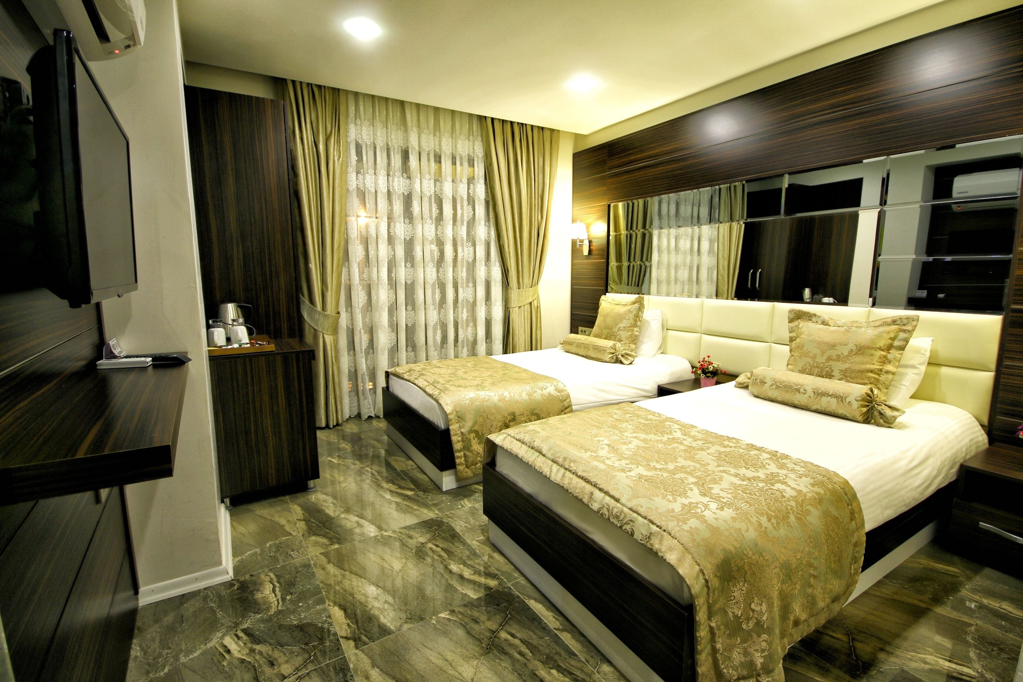 A hotel room with two beds, a TV, a minibar, and a large mirror.
