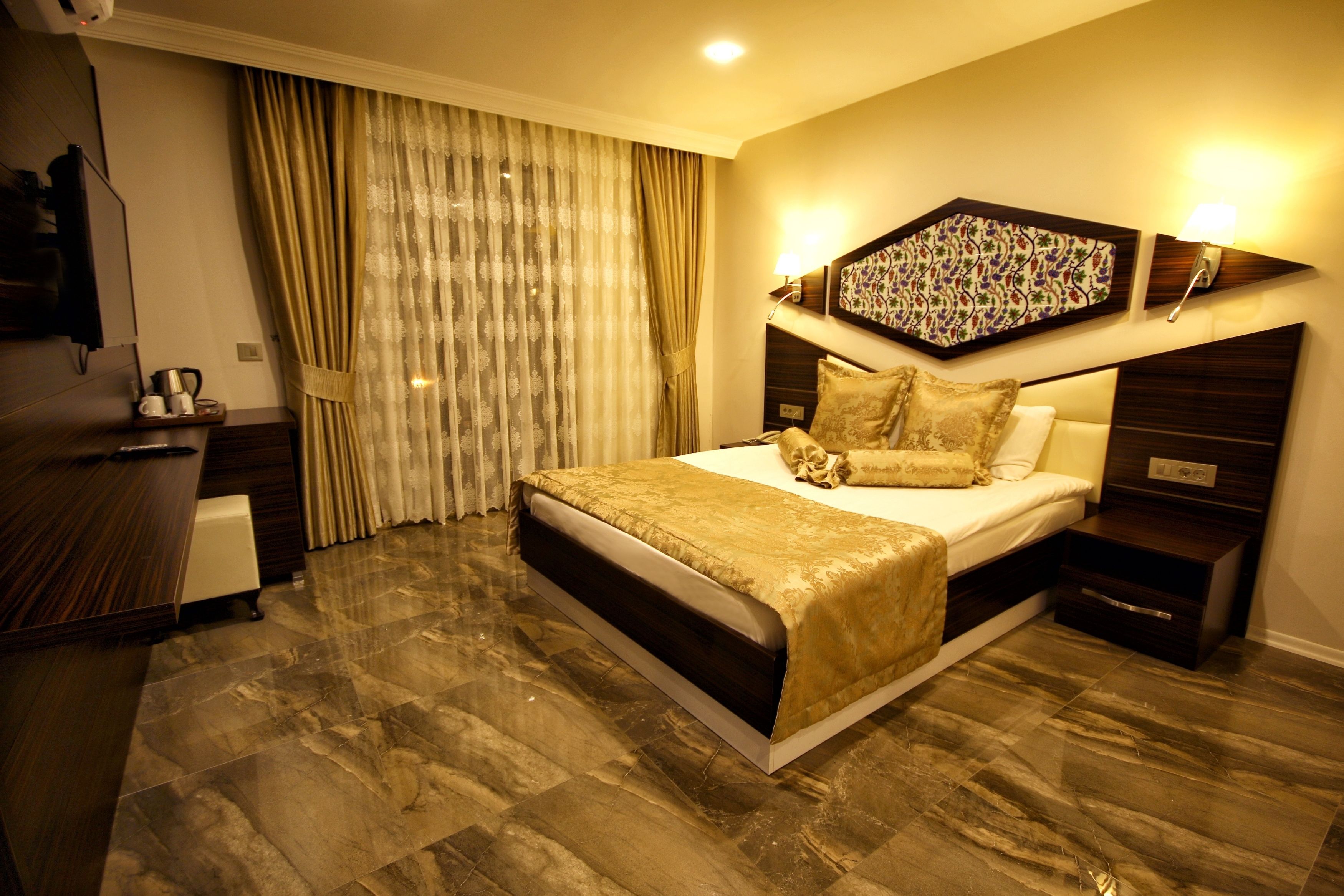 A hotel room with a large bed, a desk, a television, and a window with curtains.