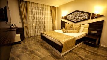 A hotel room with a large bed, a desk, a television, and a window with curtains.