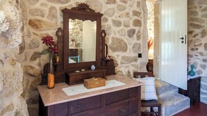 Une salle de bain aux murs en pierre, avec un meuble-lavabo en bois, un miroir et une petite commode en bois.